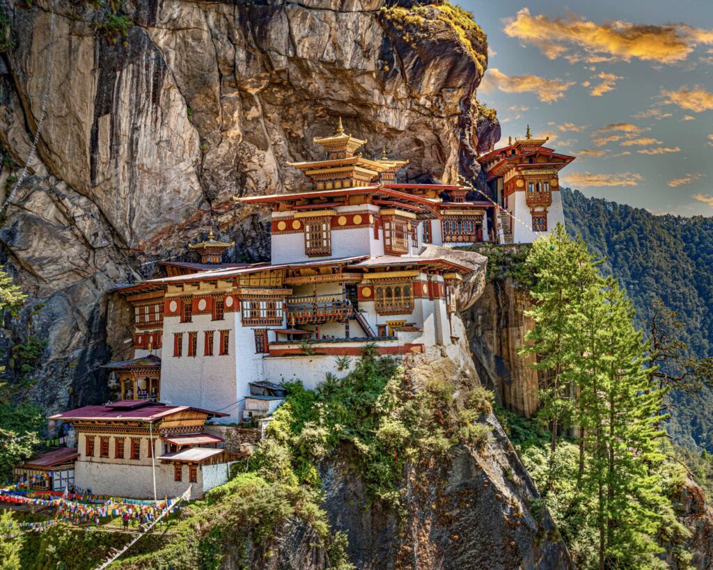 不丹著名的虎穴寺（Paro Taktsang）懸掛在峭壁上，金色屋頂與紅白相間的建築在藍天與巍峨山巒的映襯下顯得神秘而莊嚴。這座寺廟是藏傳佛教的重要聖地，吸引無數信徒與旅人前來朝拜。
