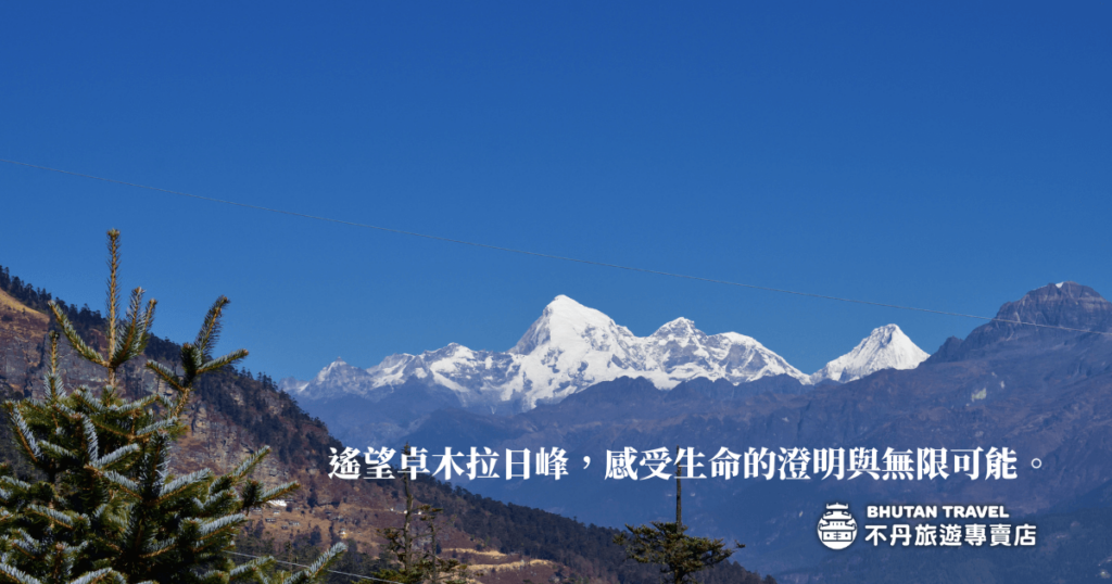 圖片展示了不丹的卓木日峰（Jomolhari）壯麗的雪山景觀，與前景中的松樹相輝映。標語「透望卓木日峰，感受生命的澄明與無限可能。」表達了大自然的震撼與心靈的澄澈，吸引那些尋求內心平靜的旅人。