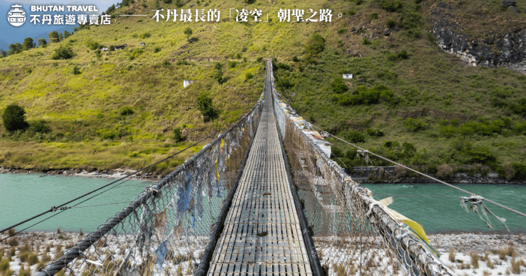 這張圖片展示了不丹的最長吊橋──普那卡懸索橋，懸掛於兩岸的高山之間，橫跨河流。吊橋的長度與其懸空的設計讓人感受到震撼與驚奇，並且其周圍的自然景觀更增添了這條朝聖之路的神聖感。橋上的五彩經文旗隨風飄動，為這片土地增添了濃厚的宗教氛圍，是朝聖者前往不丹的重要道路之一。
